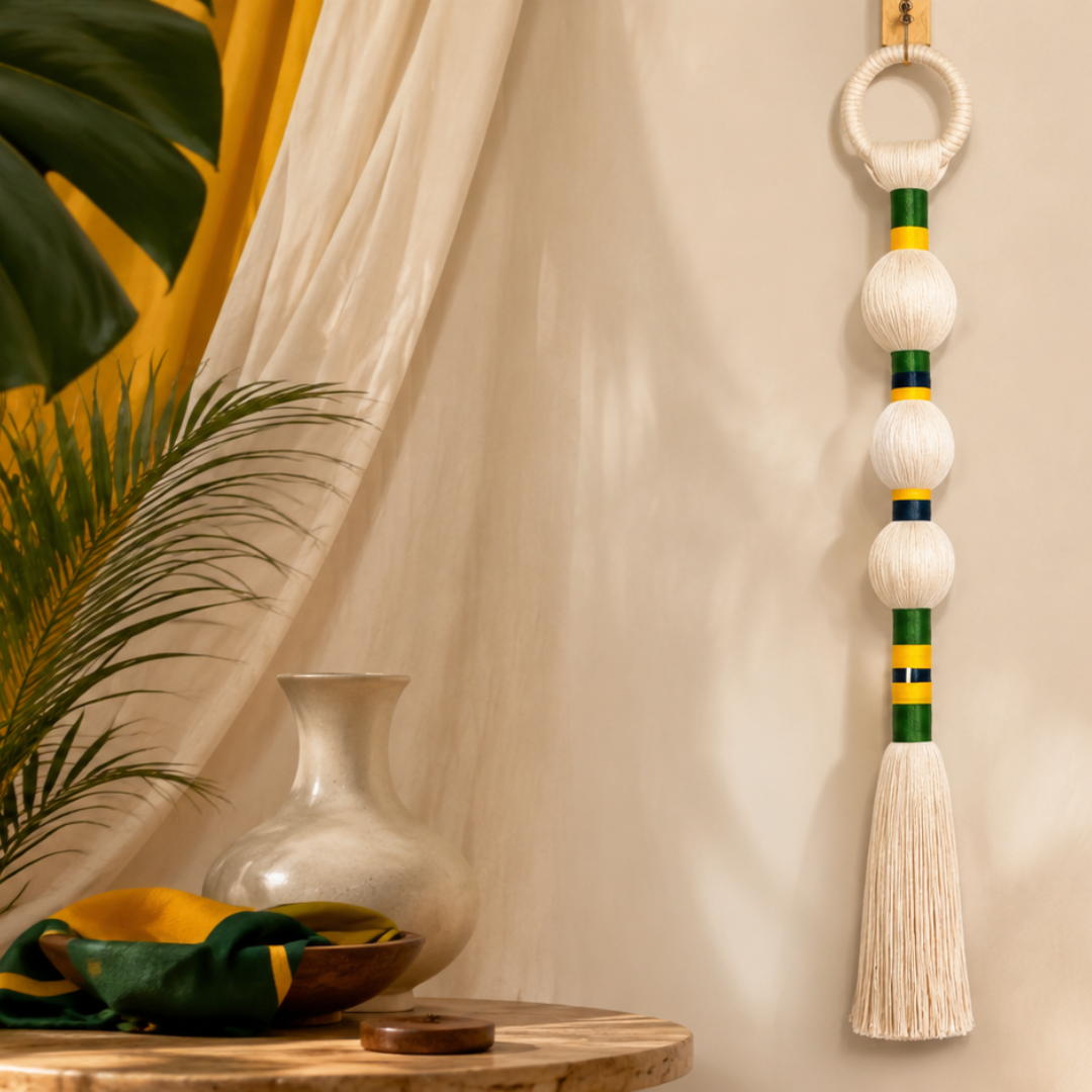 Pingente de macramê com anéis verde e amarelo ao lado de vaso e folhagem
